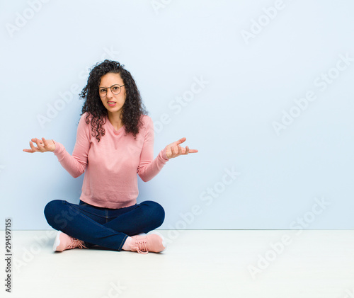 young pretty woman feeling clueless and confused, not sure which choice or option to pick, wondering sitting on floor