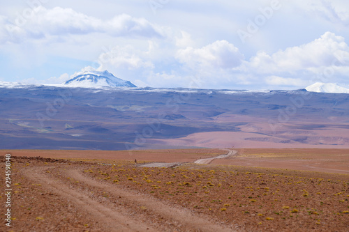 A road in the Landscape of the Bolivian highlands. Desert landscape of the Andean plateau of Bolivia with the peaks of the snow-capped volcanoes of the Andes