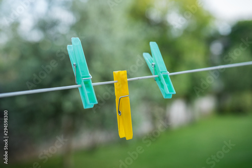 Yellow and blue clothespins with blurry green garden background. Sharp close up of those object attached to a wire. 3 practical objects made of plastic.