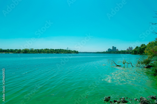 Wide river with green water with algae. River and foggy city with a bridge on the horizon