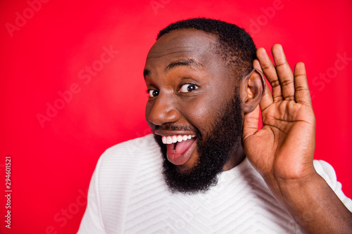Close up photo of interested curious dark skin man hold hand near ears listen confidential promo about x-mas wonder feel impressed wear style white sweater isolated over red color background photo