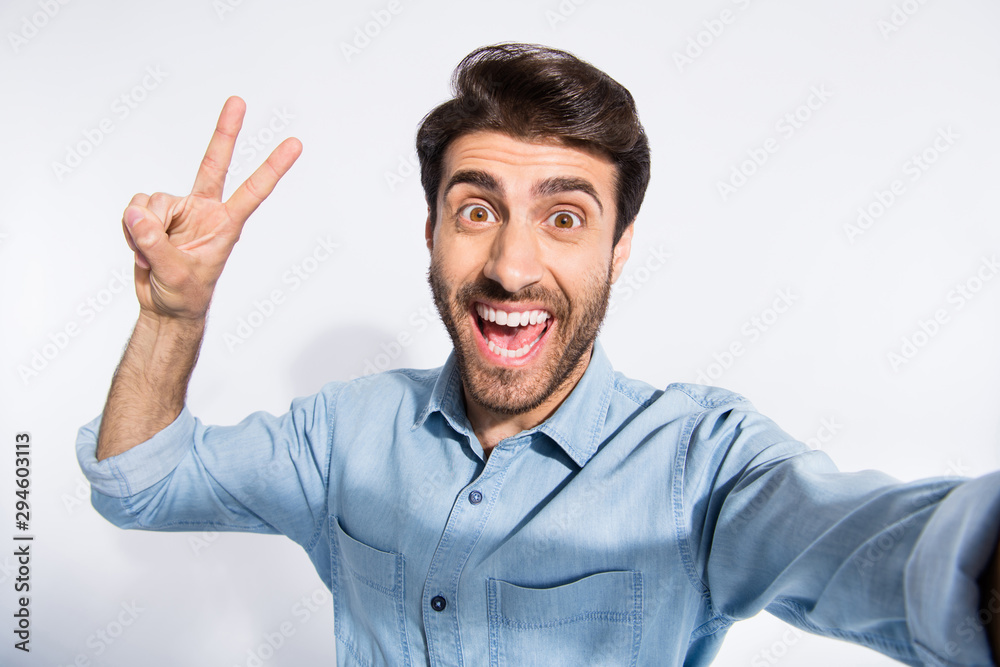 Close up photo of arabian funny guy making selfies showing v-sign symbol saying hello to friends wear casual denim shirt isolated white color background