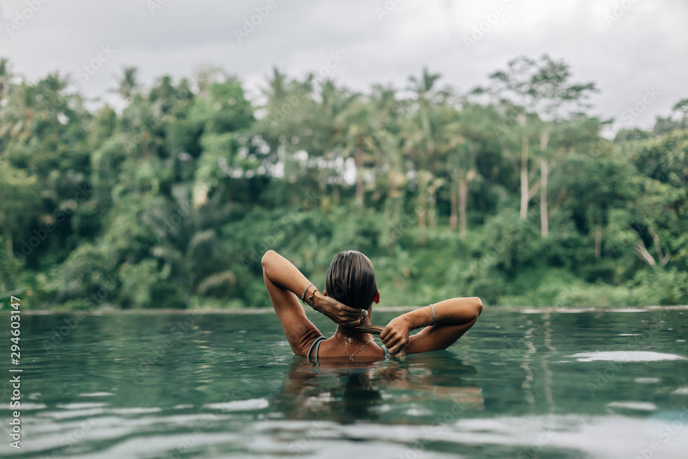 Woman enjoying tropical rain while swimming in infinity pool on Bali Woman enjoying tropical rain while swimming in infinity pool on Bali