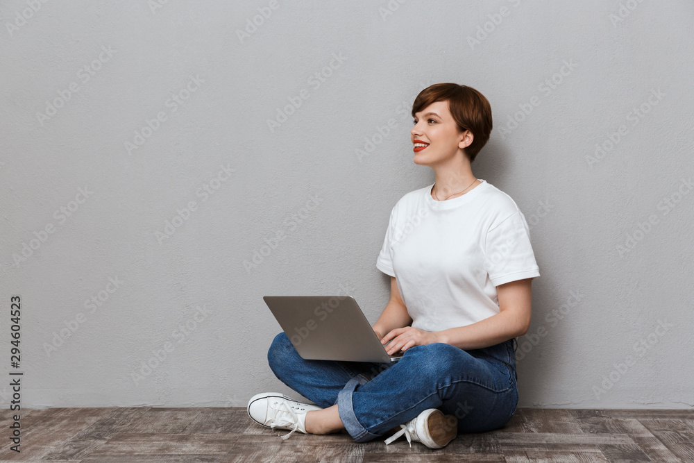 Image of pleased woman sitting on floor and using laptop computer Image of pleased woman sitting on floor and using laptop computer