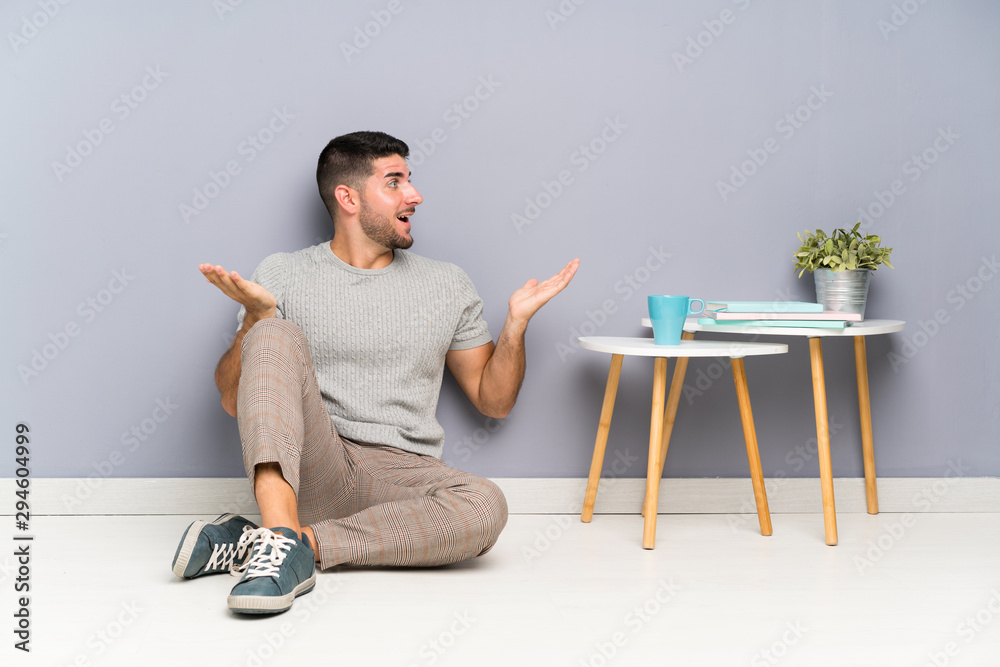 Young handsome man sitting on the floor with surprise facial expression