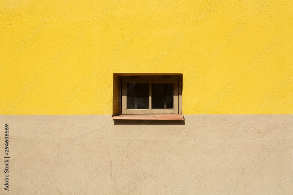Colorful wall fragment with small window in the middle background. Yellow and beige house wall on sunny summer day close up.