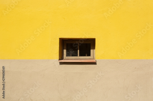 Colorful wall fragment with small window in the middle background. Yellow and beige house wall on sunny summer day close up.