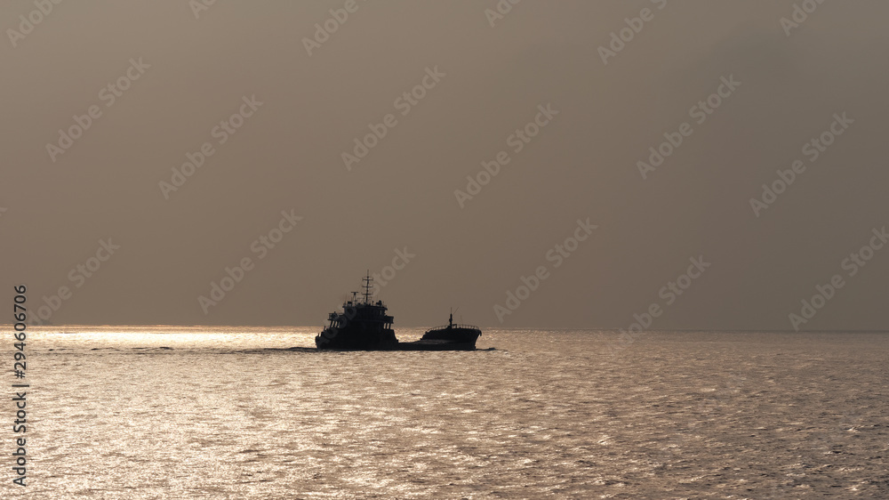 Obraz premium Cargo ship sailing on ocean in the morning with sky and sea background, Silhouette ship sailing on golden shining sea.