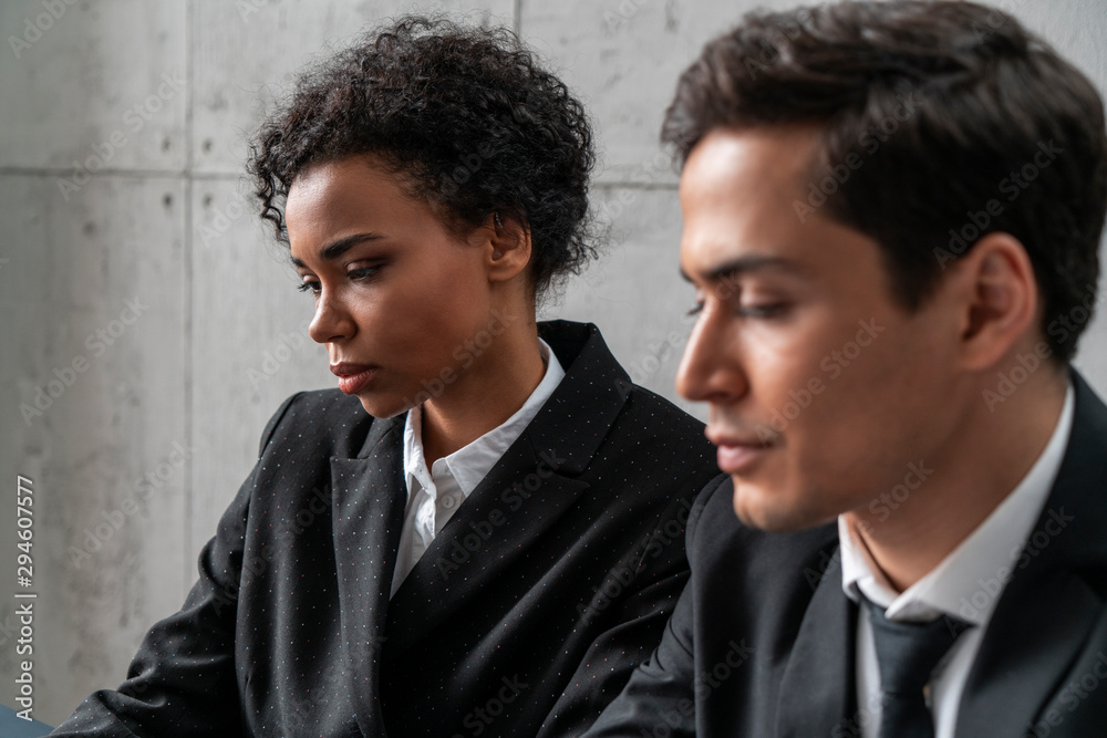 Portrait of young business people. Serious Caucasian businessman and thoughtful African American woman in background. Focus on businesswoman. Teamwork concept