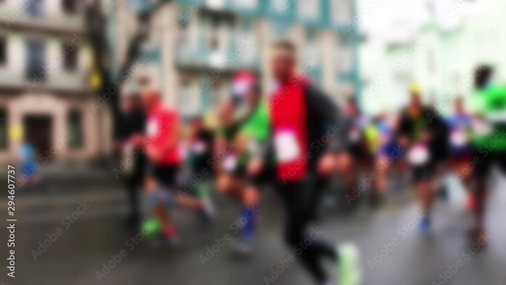 Closeup view of many blurry silhouettes of people running outdoors by city streets during charity City Marathon. Participants athletes run a long distance through the streets of the city. Slo-mo. Closeup view of many blurry silhouettes of people running outdoors by city streets during charity City Marathon. Participants athletes run a long distance through the streets of the city. Slo-mo.