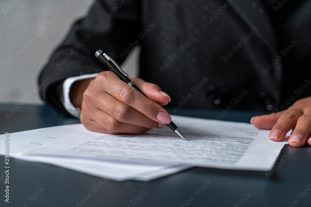Close up of African American businesswoman hand with pen and document at blurred office table. Concept of paperwork Close up of African American businesswoman hand with pen and document at blurred office table. Concept of paperwork
