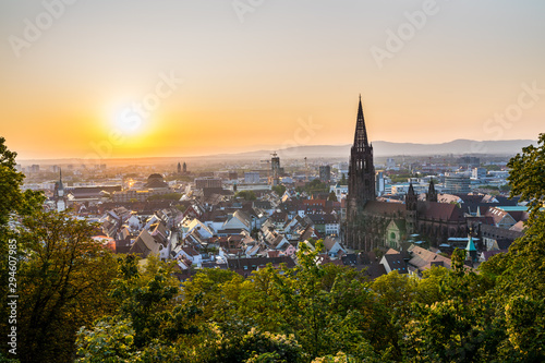 Germany  Romantic orange sunset sky decorating skyline of city freiburg im breisgau houses and cathedral seen from above  aerial view over tree tops at sunset