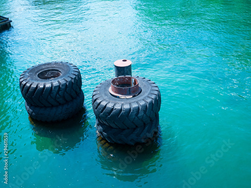 Large old black tires being used as bumpers at concrete dock, partially submerged in blue water