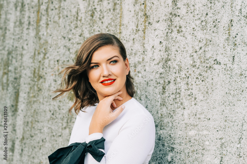 Outdoor portrait of beautiful young woman with wavy hairstyle, bright makeup red lipstick