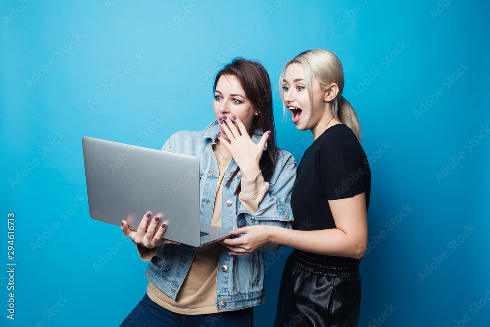 Two happy and cheerful girls dressed in fitness bodysuits, best friends have fun and watch photos on the laptop Two happy and cheerful girls dressed in fitness bodysuits, best friends have fun and watch photos on the laptop