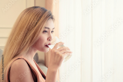 Asian woman with long hair drinking water from a glass near the window light  healthcare concept.