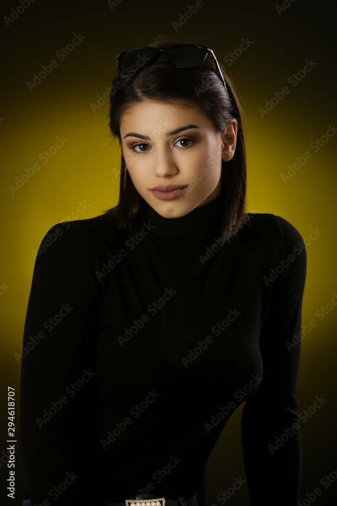 Fototapeta premium Studio portrait of a beautiful young brunette in a black shirt on a dark background, neutral facial expression