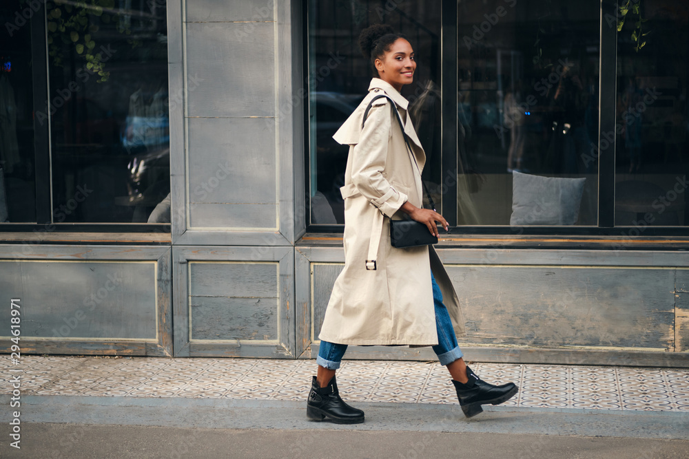 Side view of casual African American girl in trench coat happily ...