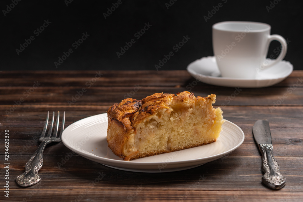 Piece of homemade traditional cornish apple pie on a white plate with a knife and fork on a wooden table. Cup of tea in the background Piece of homemade traditional cornish apple pie on a white plate with a knife and fork on a wooden table. Cup of tea in the background