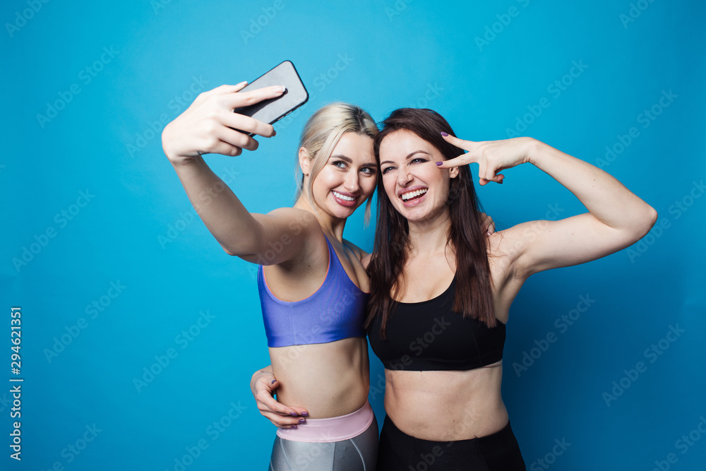 Two happy and cheerful girls dressed in fitness bodysuits, best friends have fun and take selfies Two happy and cheerful girls dressed in fitness bodysuits, best friends have fun and take selfies