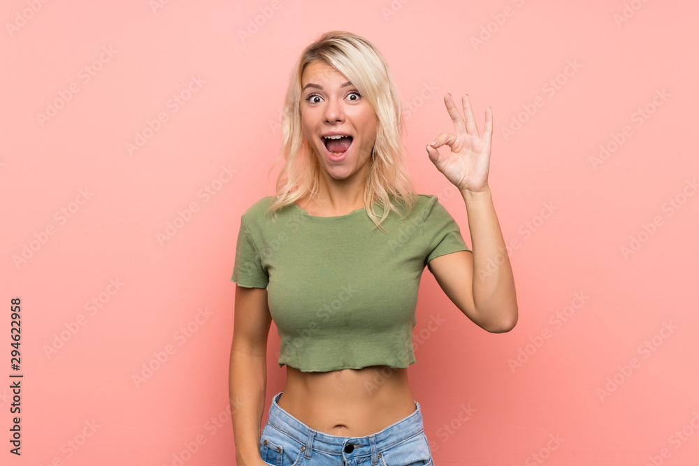 Young blonde woman over isolated pink background surprised and showing ok sign Young blonde woman over isolated pink background surprised and showing ok sign