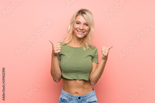 Young blonde woman over isolated pink background with thumbs up gesture and smiling