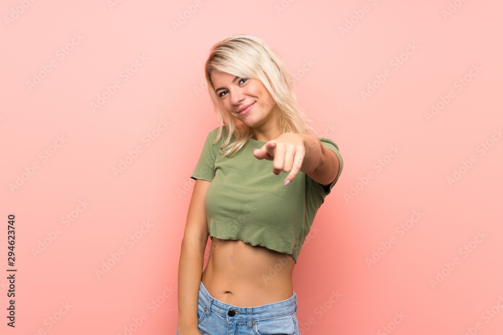 Young blonde woman over isolated pink background points finger at you with a confident expression Young blonde woman over isolated pink background points finger at you with a confident expression
