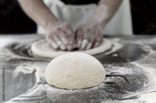 Bal van pizzadeeg op tafel met handen van de chef kneed het deeg op de achtergrond.