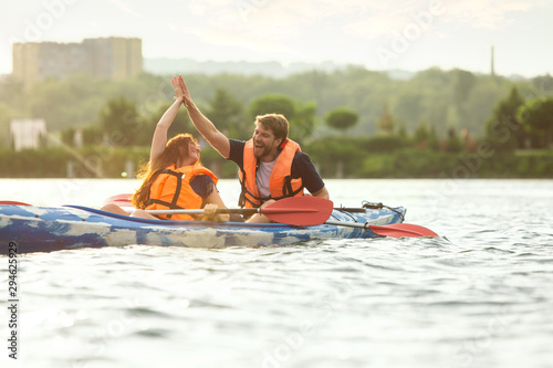 Happy young caucasian couple kayaking on river with sunset in the backgrounds. Having fun in leisure activity. Happy male and female model laughting on the kayak. Sport, relations concept. Colorful. © master1305
