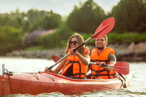 Obraz na plátně Happy young caucasian couple kayaking on river with sunset in the backgrounds