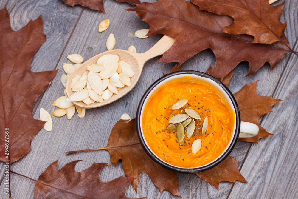 Fototapeta premium Vegetarian autumn pumpkin cream soup with seeds with autumn leaves.