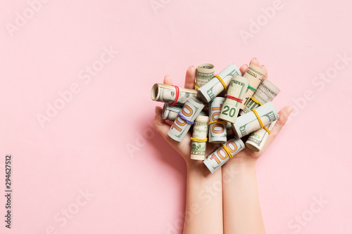 Top view of female hands holding a lot of rolled up dollar banknotes on colorful background. Poverty concept. Credit concept