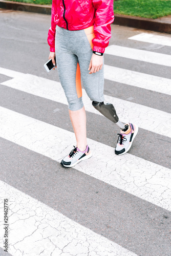 partial view of disabled sportswoman with prosthesis holding smartphone on street