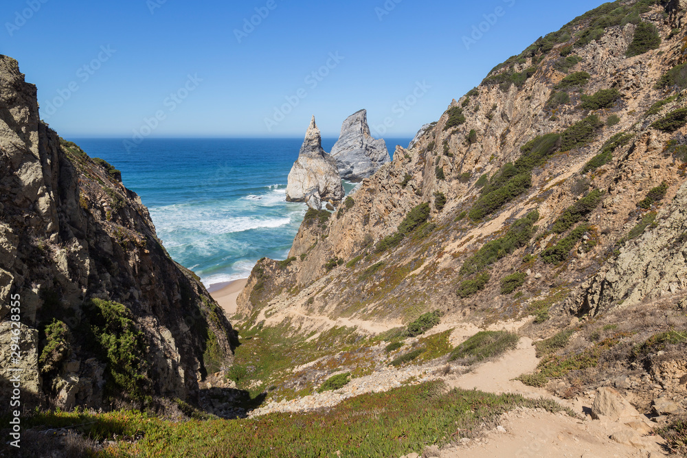 Scenic view of the Atlantic Ocean, rugged coastline with huge boulders and trail to the Praia da Ursa beach near Cabo da Roca, the westernmost point of mainland Europe, in Portugal.
