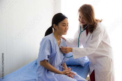 Beautiful Asian woman doctor check heartbeat with stethoscope on young woman patient's chest and listen unusual rate in hospital