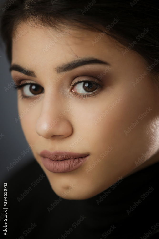 Studio portrait of a beautiful young brunette in a black shirt on a dark background, neutral facial expression