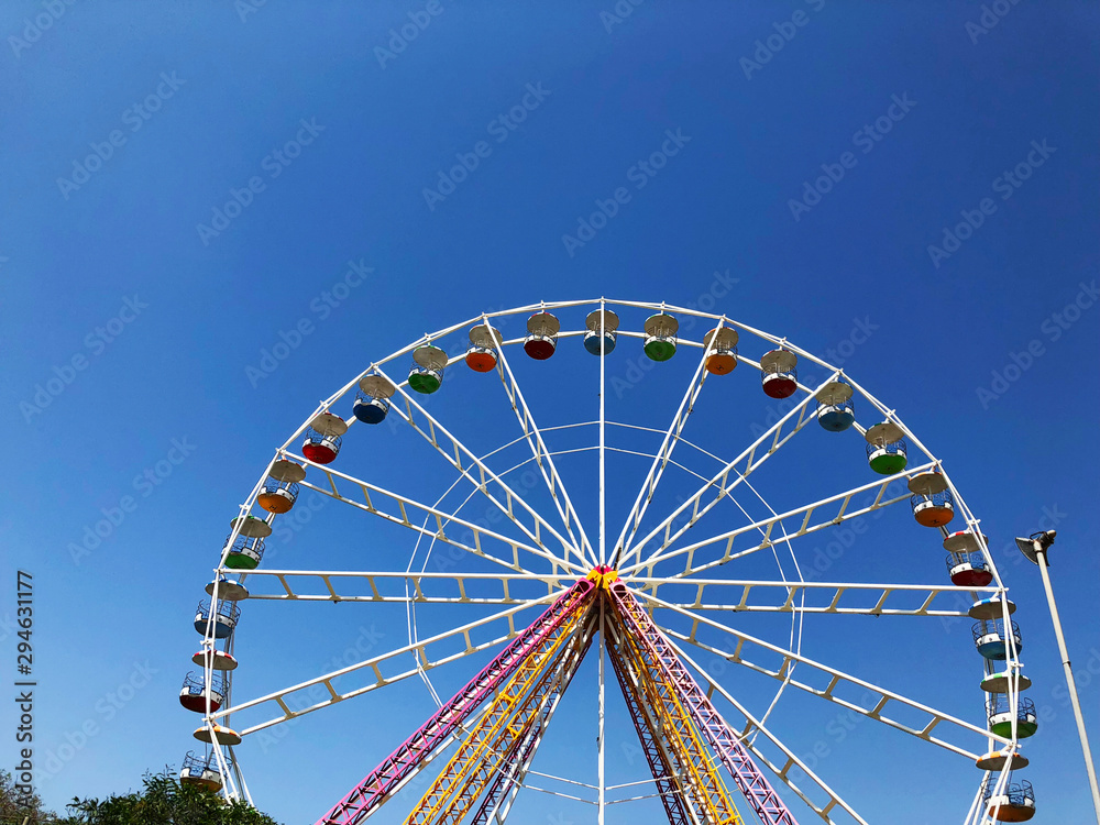 A large white Ferris Wheel with a skyscraper in the background is highlighted against a blue sky