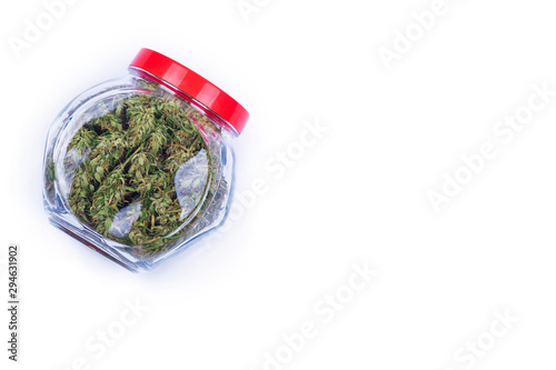 Top view of fresh green buds or flowers of cannabis marijuana weed in a transparent glass jar isolated on white background. Alternative treatment. Medical cannabis. Copy space.