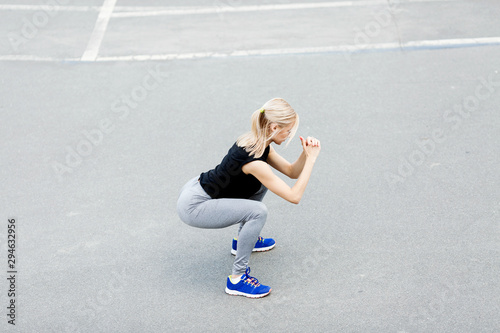 Fototapeta Naklejka Na Ścianę i Meble -  Burn in buttocks. Side view of young woman in sportswear doing squat . Young beautiful woman squats