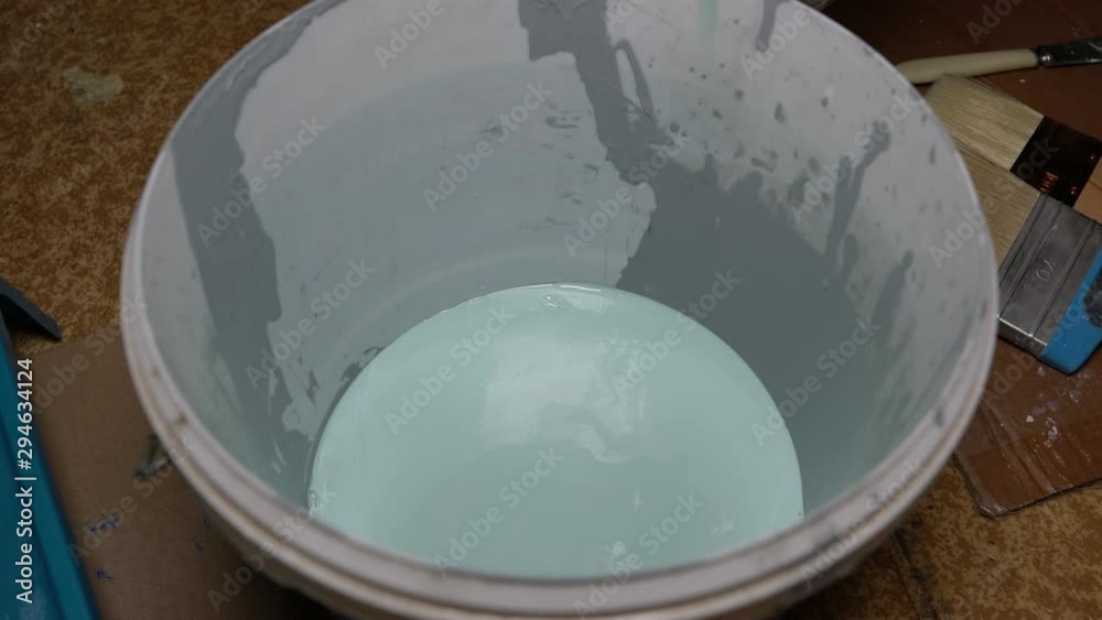 Turquoise paint is poured into a white plastic bucket Turquoise paint is poured into a white plastic bucket