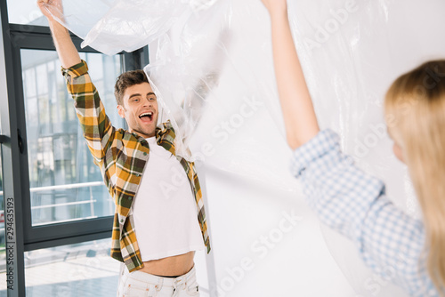 happy young man holding cellophane with girlfriend while preparing for room repair
