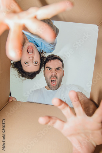 Curious wife and husband unpacking, reaching things from carboard box, looking inside, roaring like monsters.