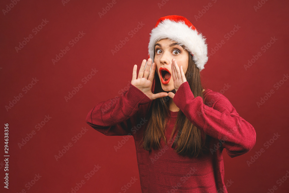 Screaming about the news. Christmas Santa hat woman portrait. Smiling amazed happy girl isolated against red background. Free copyspace for text. New year concept. Screaming about the news. Christmas Santa hat woman portrait. Smiling amazed happy girl isolated against red background. Free copyspace for text. New year concept.