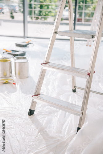 selective focus of ladder in room with cans of paint on white floor covered with cellophane