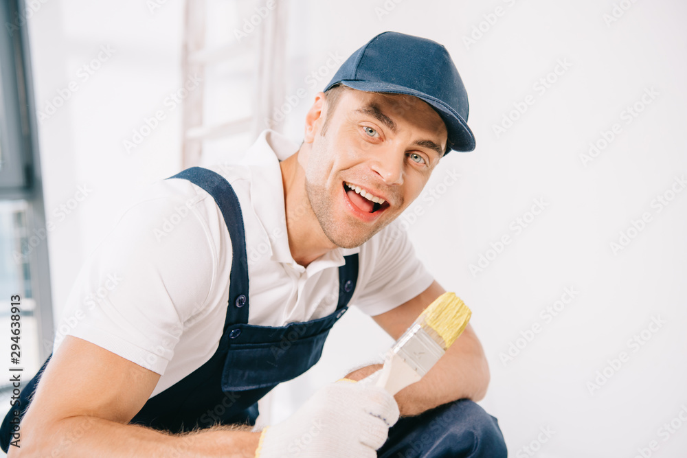 cheerful young painter in uniform holding paintbrush and smiling at camera cheerful young painter in uniform holding paintbrush and smiling at camera
