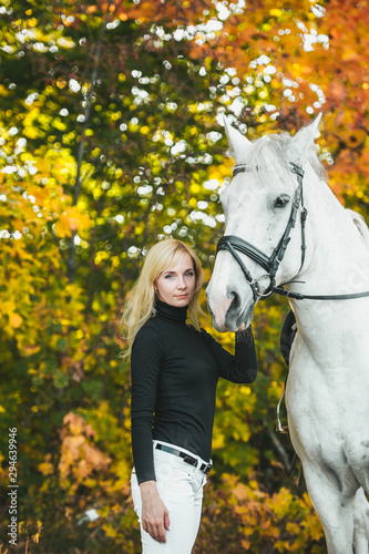 Pretty young woman with a white horse riding in autumn day