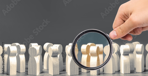 A magnifying glass looks at a crowd of wooden figures of people. society, demographic. group of citizens, rally, political movement or electorate. Customers and buyers, preferences of Population.
