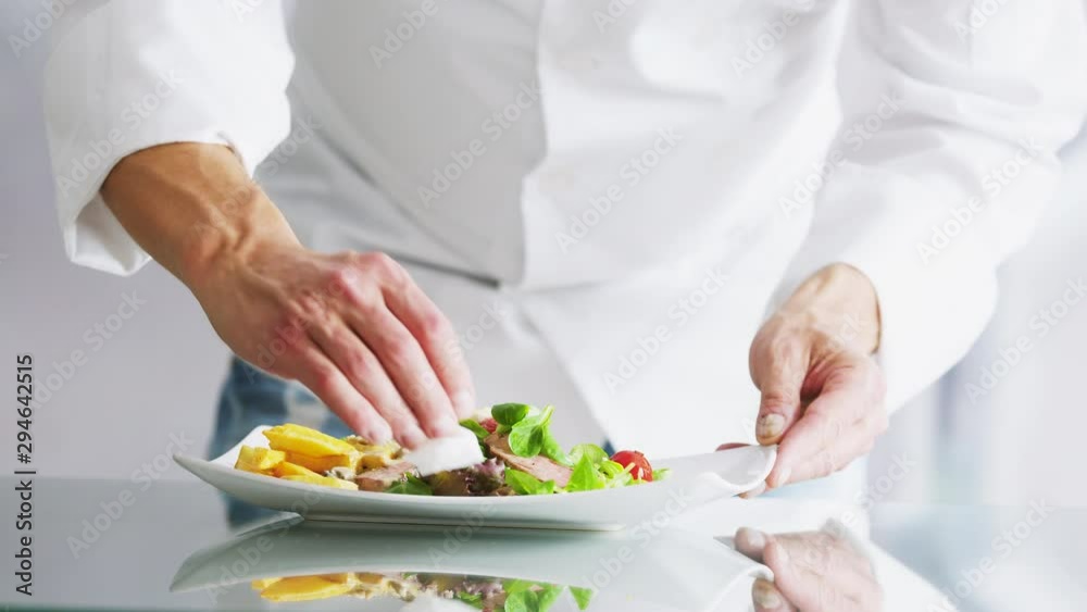 Chef professional cleans the plate with a cloth and decorating meal. Cook preparing salad with beef meat. Chef professional cleans the plate with a cloth and decorating meal. Cook preparing salad with beef meat.