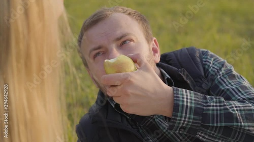 Close-up of caucasian man talking to his daughetr ad eating apple. Young blonde girl spending time with her father on the autumn meadow. photo