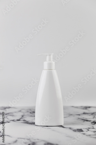 Blank empty moisturizer container on white background on marble table. Cosmetic plastic bottle of cream or lotion, empty without a label © Olha